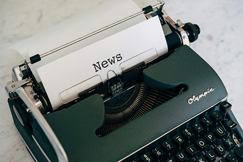 a green typewriter with a paper loaded and the top headline reading "News" the rest of the paper is in the typing que to be filled.